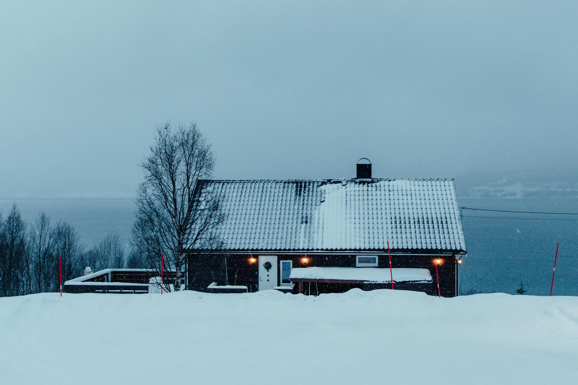 a house is covered in snow and has a lake in the background